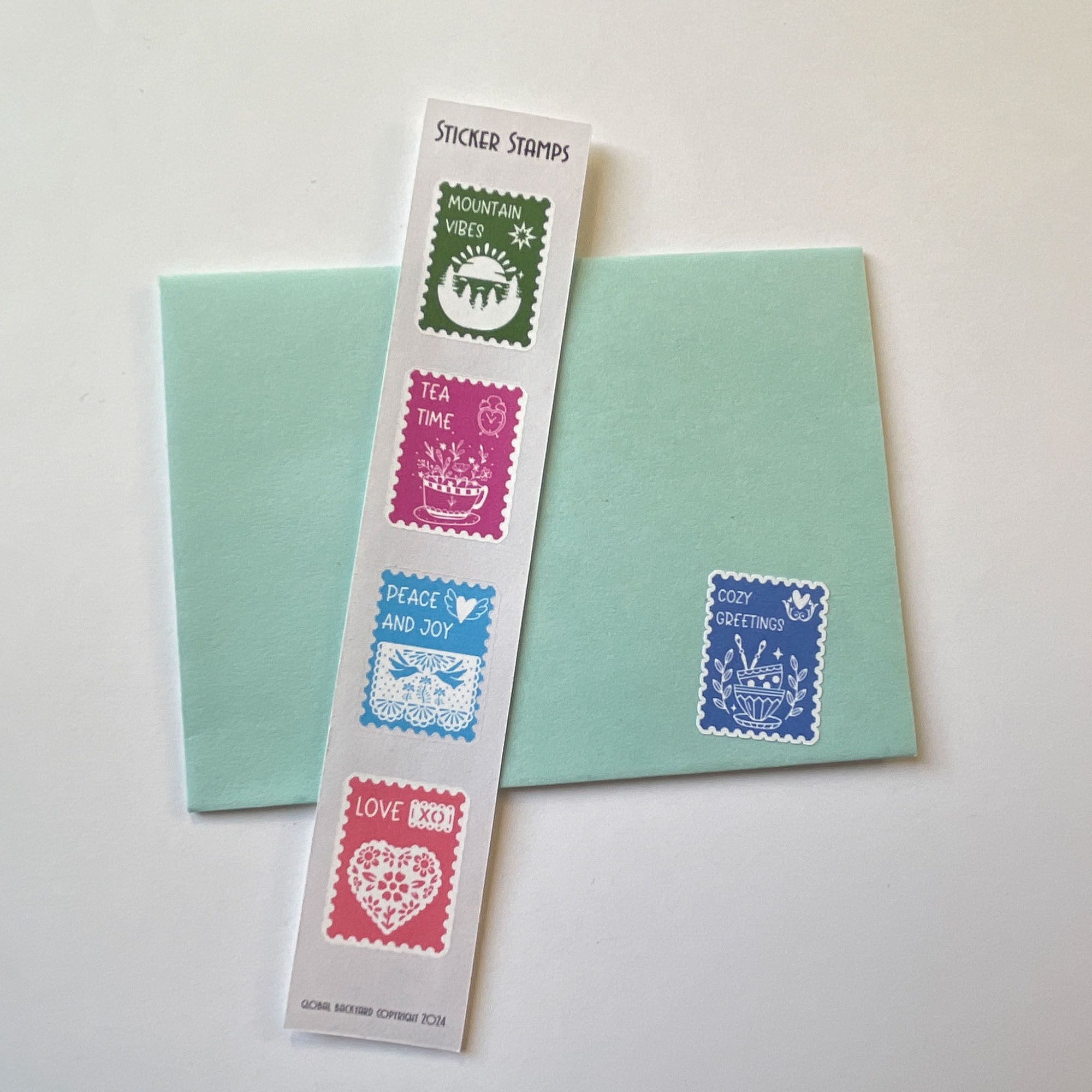 Postage stamp art sticker sheet of four, including Mountain Vibes, Tea Time, Peace and joy, Love. Cozy Greetings sticker shown on envelope which comes on a different sticker sheet.